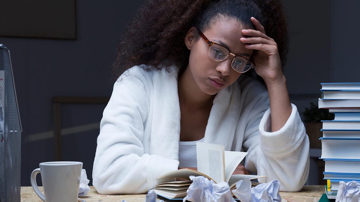 A frustrated medical school student studying for the USMLE in front of a pile of textbooks.